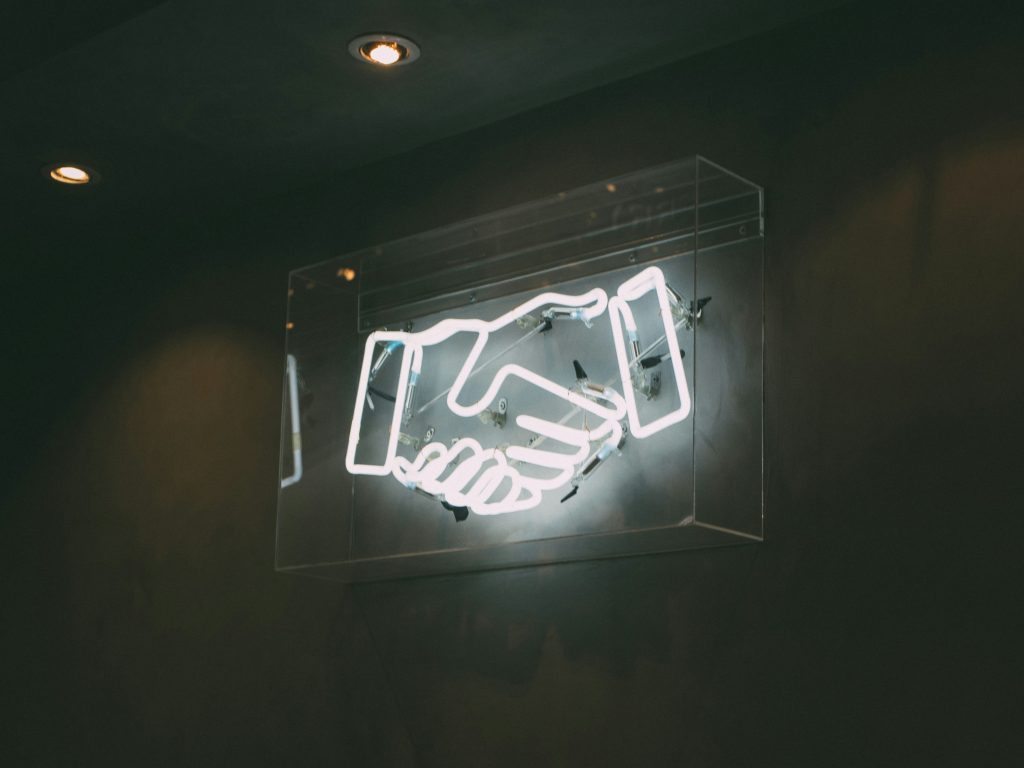 Neon lights of two hands shaking - representing partnership in research.